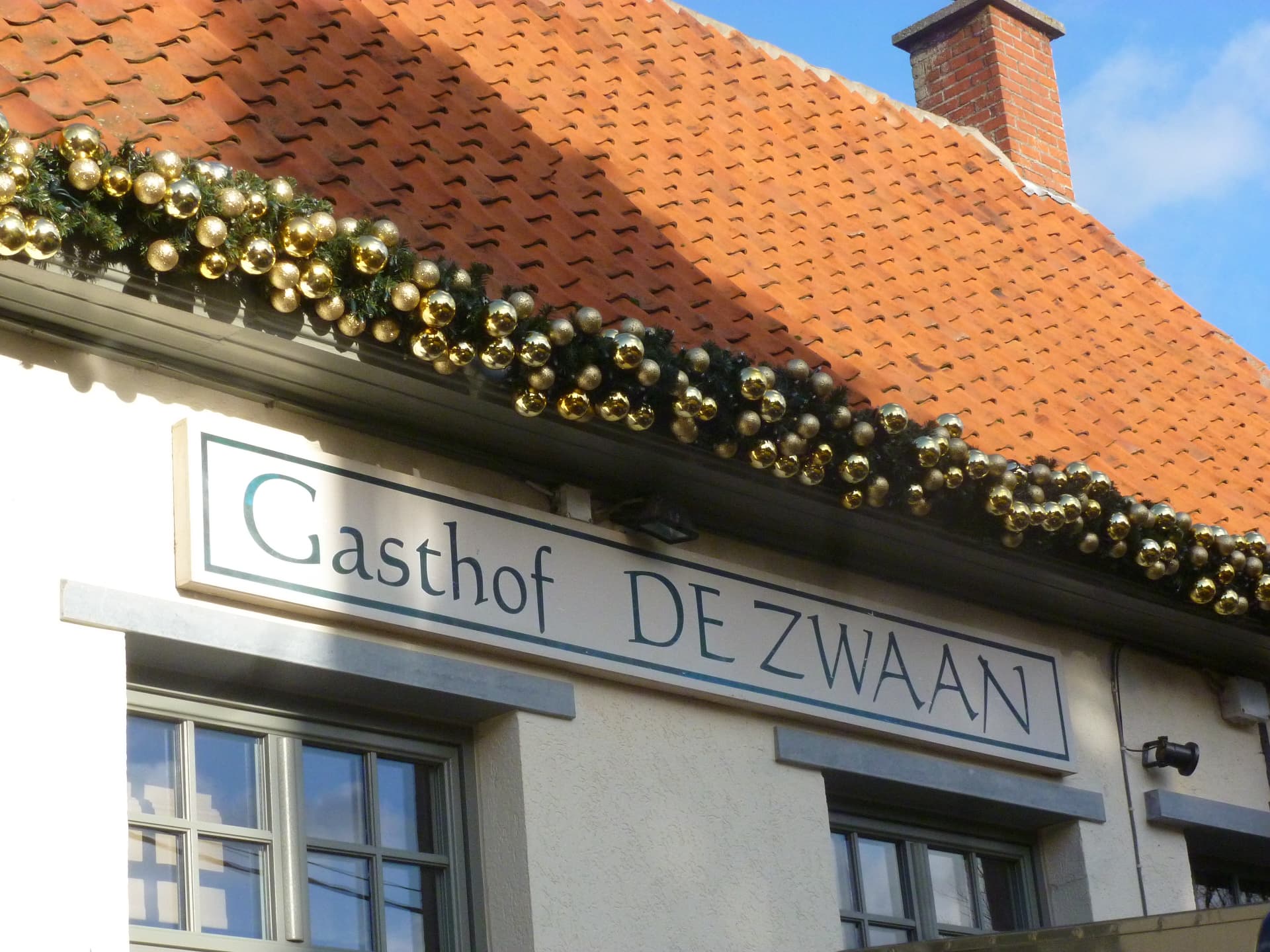 Guirlande met gouden kerstballen langs een horecagevel