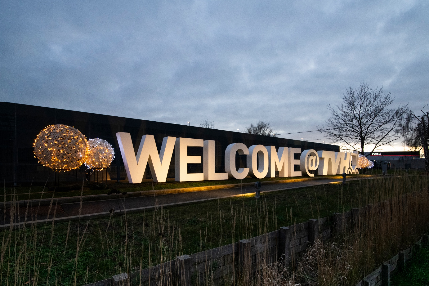 Kerstballen naast het WELCOME @ TVH-signage bij schemer